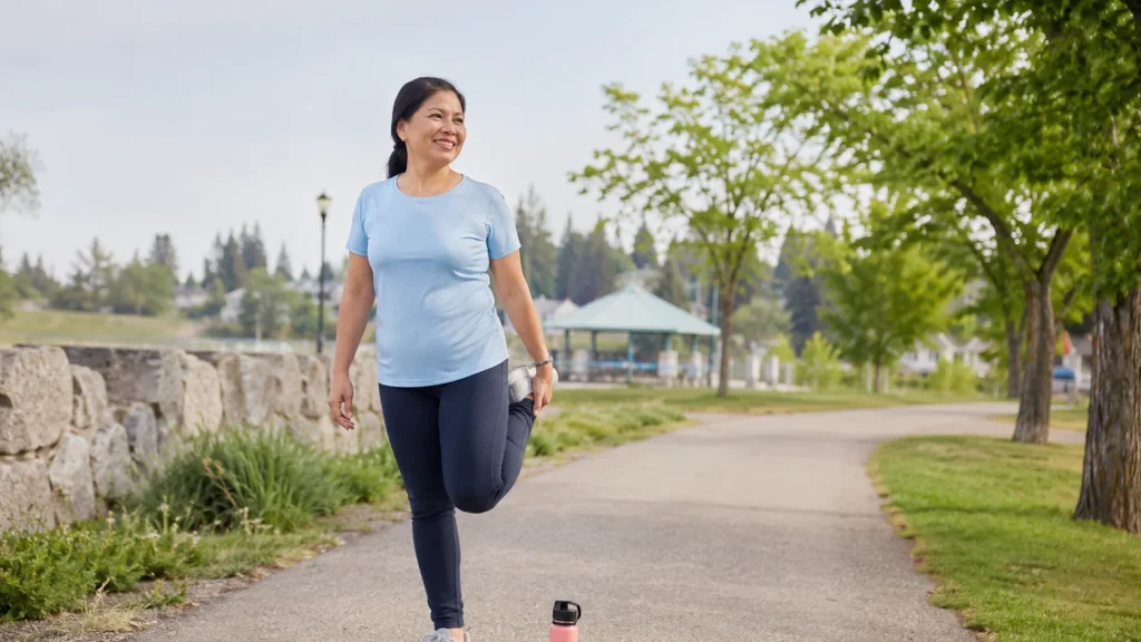 A woman in a light blue shirt walking on a tree-lined path outdoors.